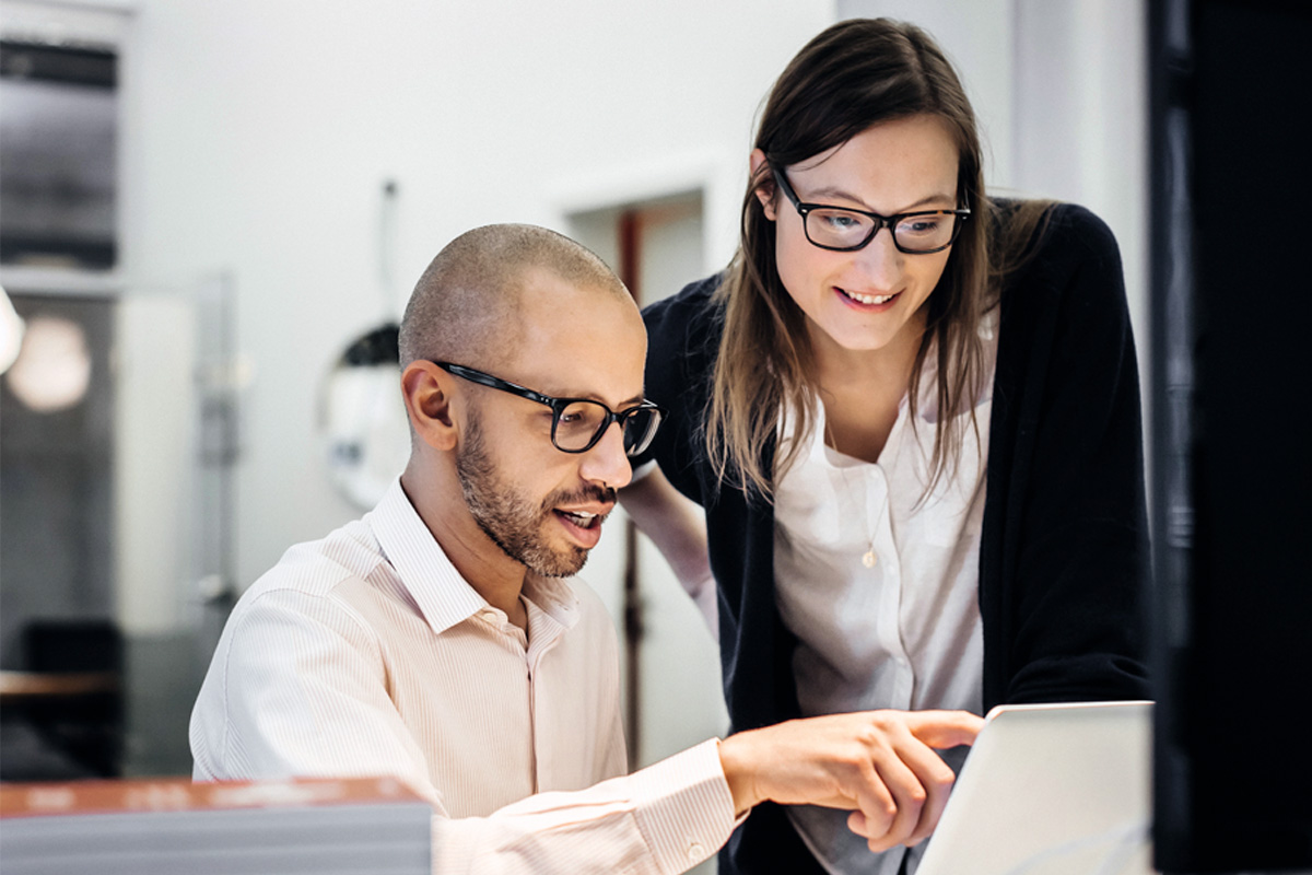 Mann und Frau besprechen im Büro etwas und zeigen auf einen laptop