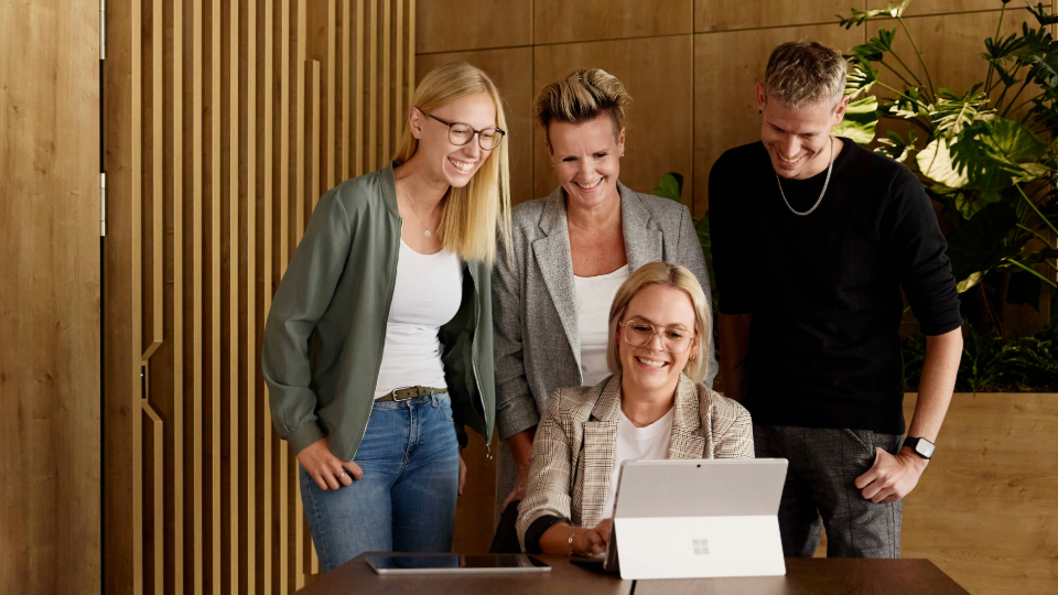 Menschen stehen nebeneinander und schauen gemeinsam auf einen Laptopbildschirm in einem Büro
