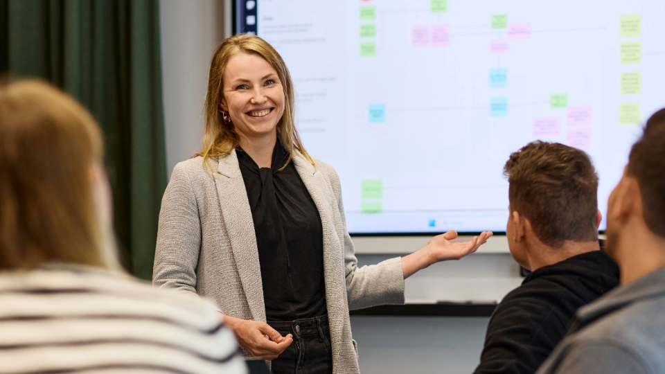 Mitarbeiterin aus der IT Abteilung steht vor einer Gruppe und hält eine Präsentation und lächelt dabei in die Kamera