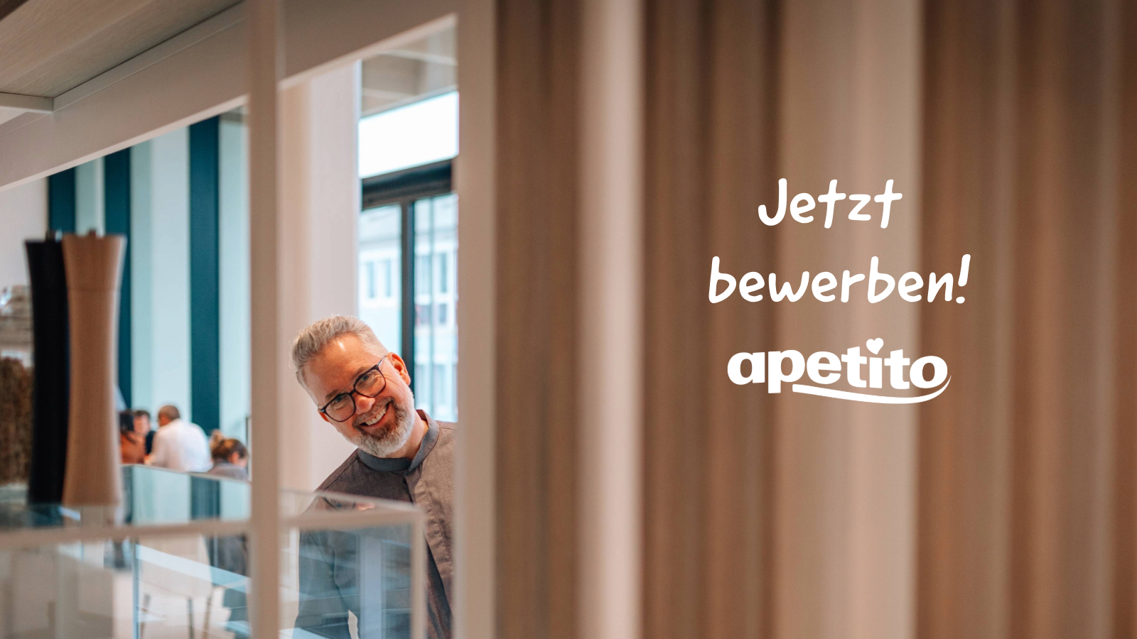 Mann der hinter einem Pfeiler nebenher schaut und in die Kamera lächeln, auf dem Bild ist ein Slogan "Jetzt Bewerben!" zu sehen