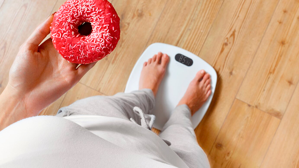 Frau-auf-einer-Waage-mit-einem-Dounut-in-der-Hand