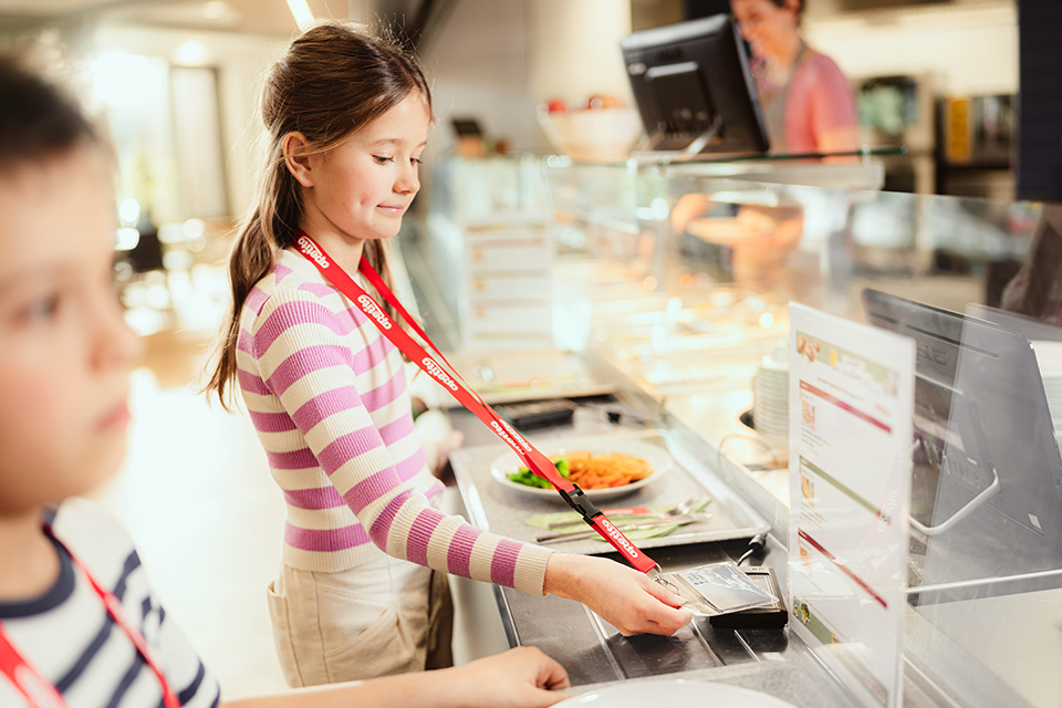 Mädchen steht lächelnd an der Kasse einer Essensausgabe