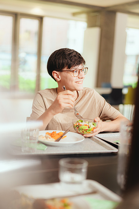 Junge isst Salat und schaut lächelnd zur Seite