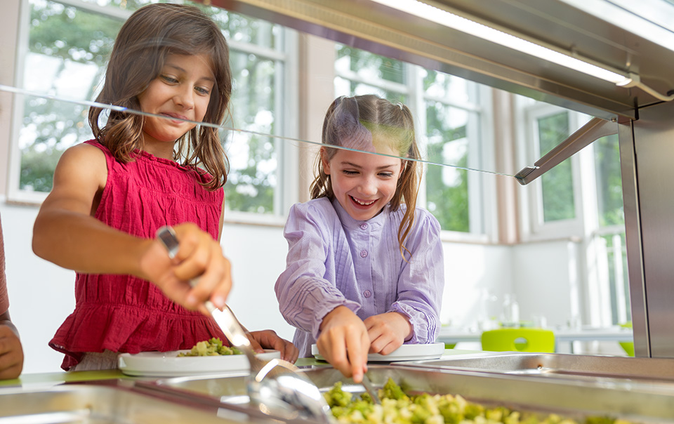 Zwei Mädchen nehmen sich an der Essensausgabe selbständig Essen
