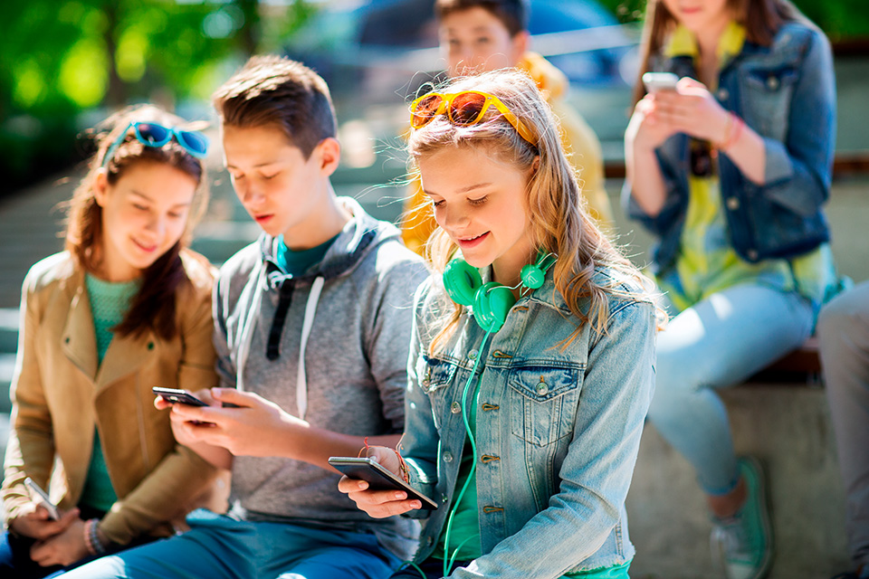 Drei Jugendliche sitzen draußen auf dem Pausenhof mit ihren Smartphones in der Hand