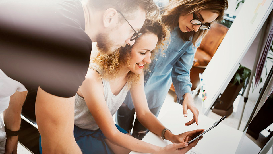 Drei-Menschen-an-einem-Schreibtisch-schauen-gemeinsam-auf-ein-Tablet