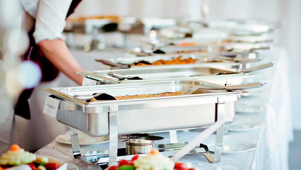 Mit-Essen-gefuellte-Gastronormbehaelter-als-Buffet-auf-einem-langen-Tisch