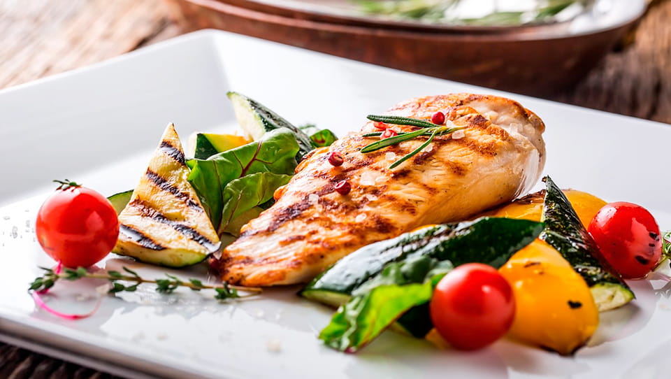 Gegrilltes-Haehnchenfilet-angerichtet-auf-einem-eckigen-weissen-Teller-mit-Grillgemuese-Rosmarin-grobem-Salz-und-Pfefferkoernern