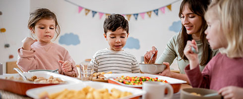 Drei-Kinder-mit-Erzieherin-beim-Mittagessen-in-der-Kita
